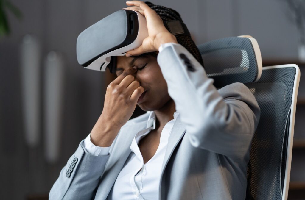 A woman pinches bridge of her nose in discomfort while removing her virtual reality headset.