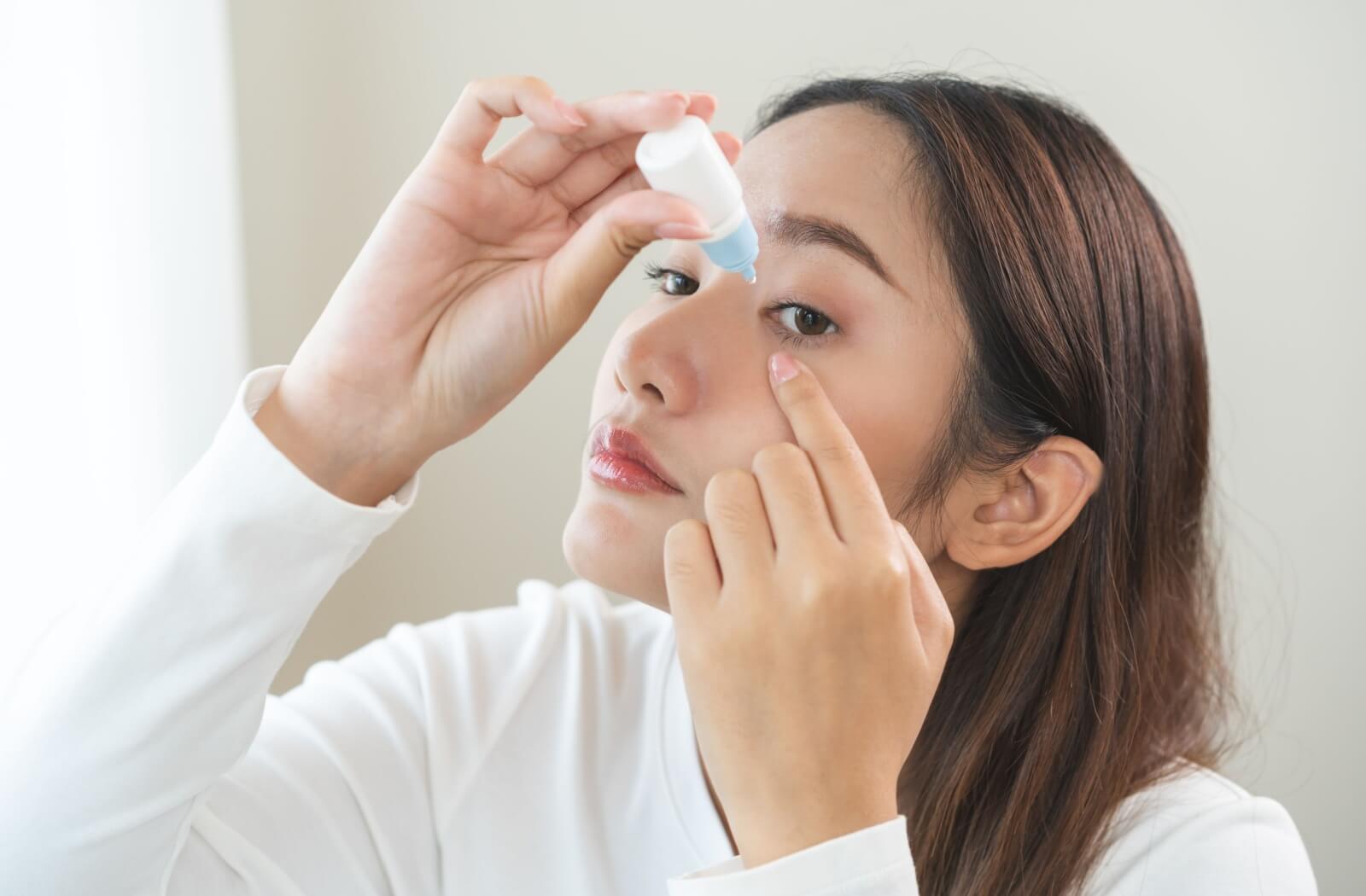 A person pulls down their eyelid to carefully apply eyedrops and treat their dry eyes.